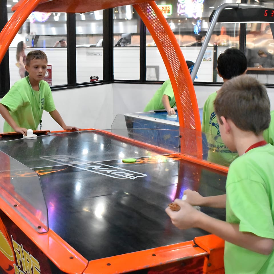 Kids in bright green shirts playing air hockey at Decades Family Restaurant.
