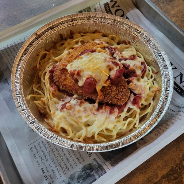 Chicken Parmesan with spaghetti and melted cheese in a foil container on newspaper.