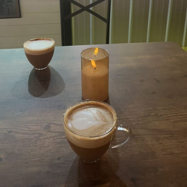 Two coffees with latte art and a flickering candle on a dark wooden table at Decades Family Restaurant.