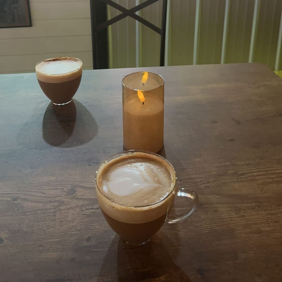 Two coffees with latte art and a flickering candle on a dark wooden table at Decades Family Restaurant.
