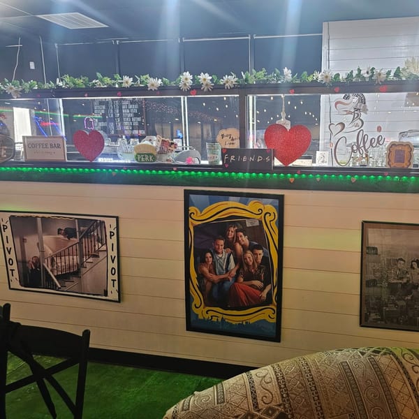 A coffee bar with a menu, Friends-themed decor, and framed pictures on a white paneled wall.