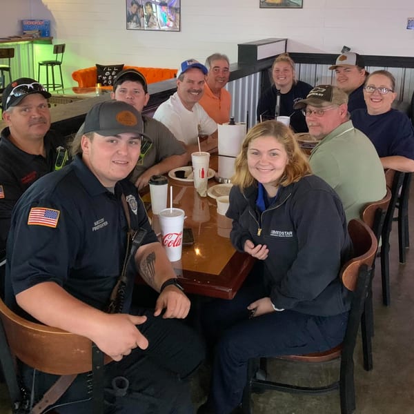 A group of ten people, including first responders, smiling around a table at Decades Family Restaurant.