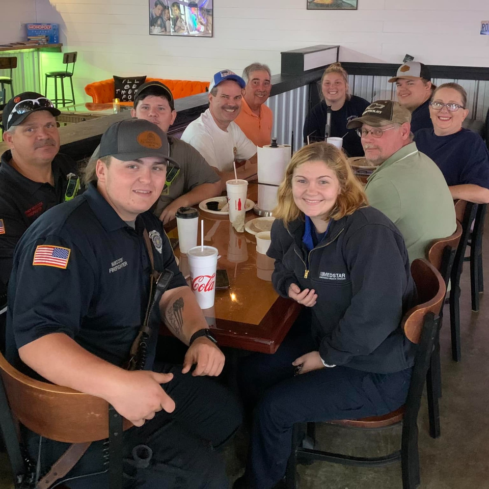 A group of ten people, including first responders, smiling around a table at Decades Family Restaurant.