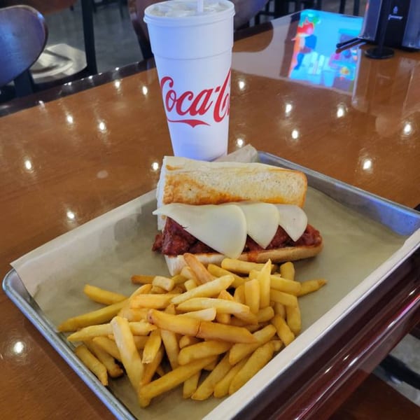 Meatball sub with melted cheese, fries, and a Coca-Cola drink on a metal tray at Decades Family Restaurant.