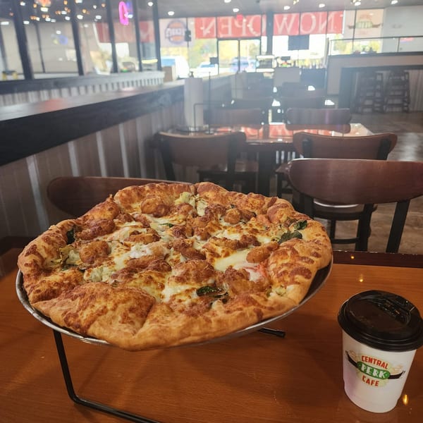 A Decades Family Restaurant pizza with a thick crust and a Central Perk Cafe cup on a table.
