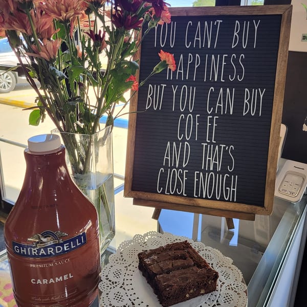 A Ghirardelli caramel sauce bottle, brownie, flowers, and a letter board with a coffee quote.