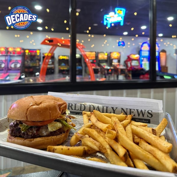 A burger and fries on a tray with a newspaper, arcade games visible in the background.