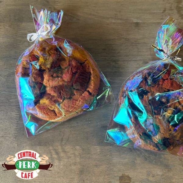 Two individually wrapped cookies in iridescent bags with ribbons, on a wooden surface.