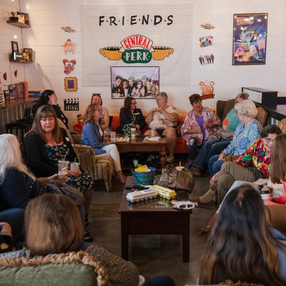 Women gathered in a cozy restaurant lounge area with Friends TV show decor on the wall.
