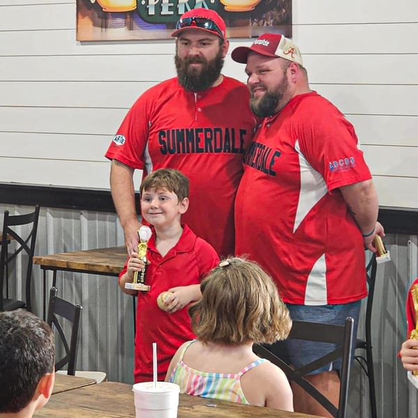 Two men in red baseball jerseys and a child holding a trophy at Decades Family Restaurant.
