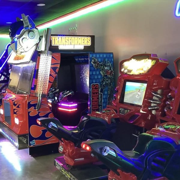 Arcade games, including a Transformers truck and motorcycle racing games, under neon lights.