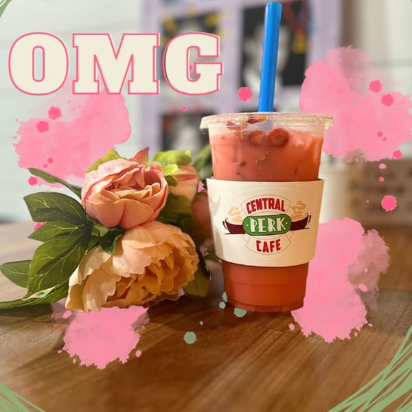 A pink drink with a blue straw and "Central Perk Cafe" sleeve, next to pink flowers.