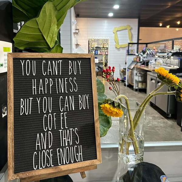 A letter board sign with a coffee quote, sunflowers, and red berries in a vase at Decades Family Restaurant.