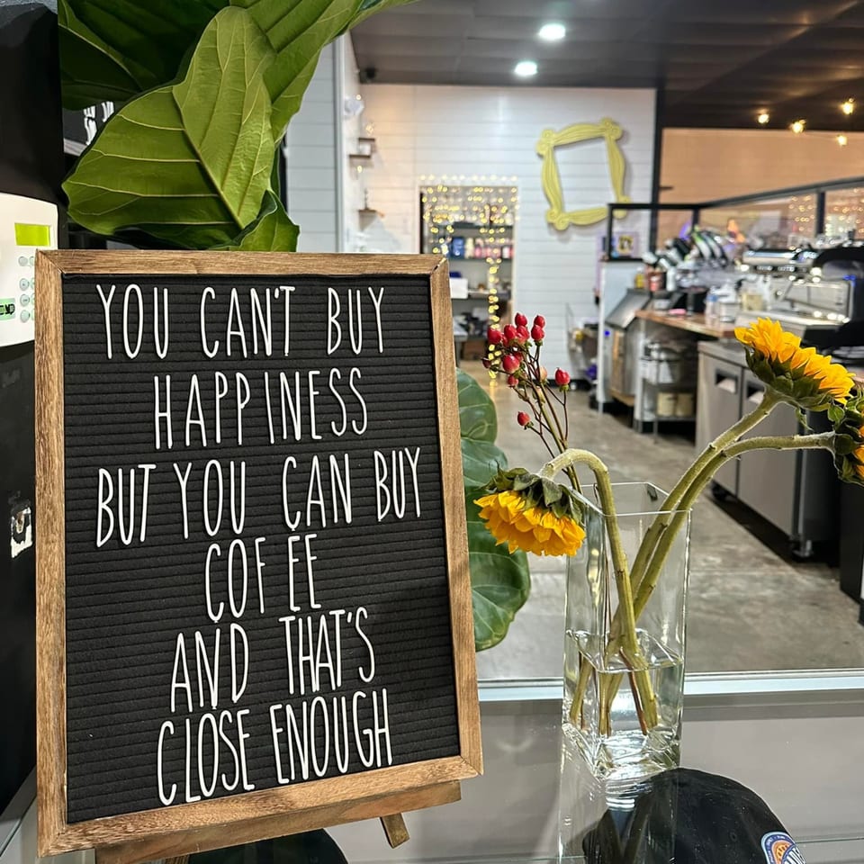 A letter board sign with a coffee quote, sunflowers, and red berries in a vase at Decades Family Restaurant.