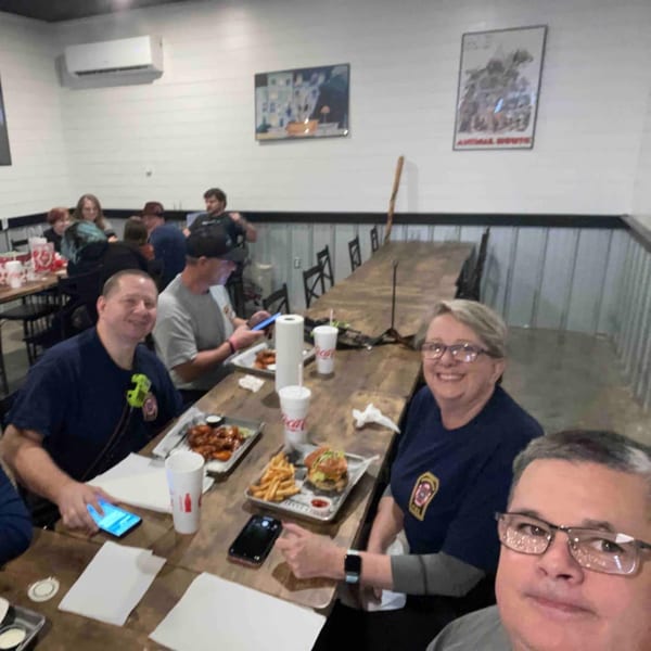 Diners enjoying burgers, fries, and wings at long wooden tables inside Decades Family Restaurant.