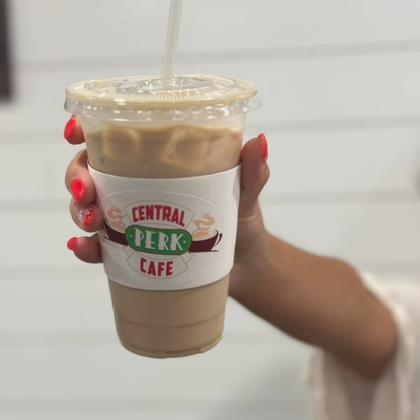 A hand with red nails holds an iced coffee in a Central Perk Cafe branded cup.