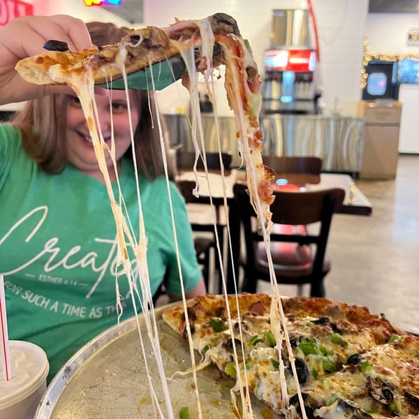 A person holds a slice of Decades Family Restaurant pizza with long, stretchy cheese pulls.