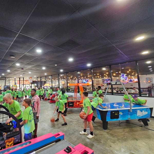 Kids in green shirts playing arcade games, including basketball and air hockey, at Decades Family Restaurant.